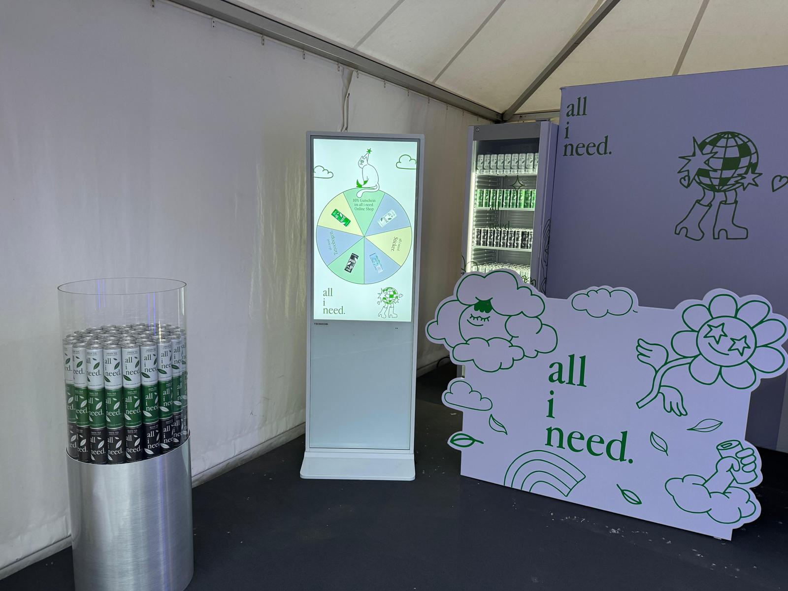 all i need Glücksrad auf dem digitalen Terminal neben gekühlten Eistee Dosen am Stand